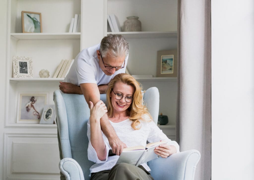 A couple happily talking and reading together in a cozy, inviting room. Their joyful moment reflects the satisfaction of moving up in their new lease to own home in Raleigh.