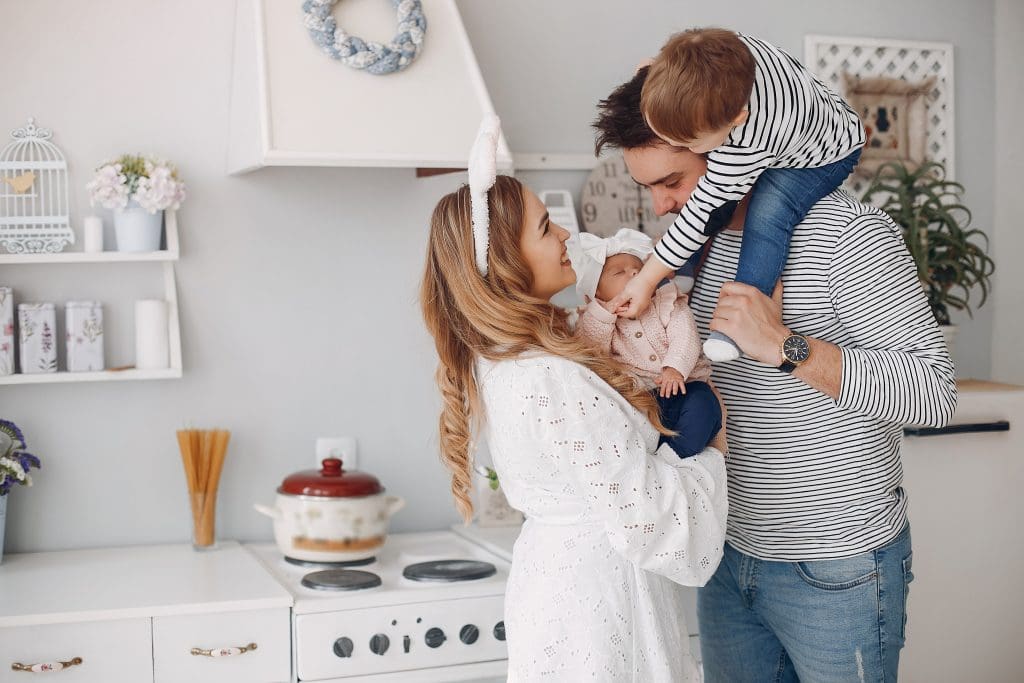 Smiling young mother and father with toddler on the husband's shoulders standing in the kitchen of their new equity-building lease to own home in Raleigh, NC