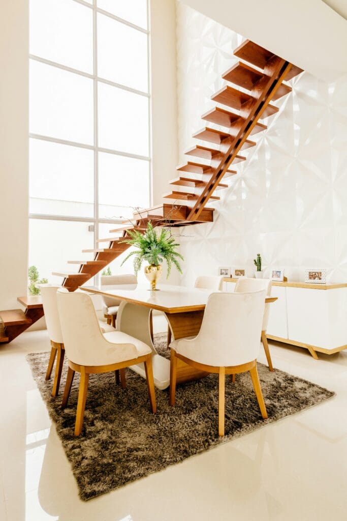 A stylish dining area featuring a dining table with matching chairs, set on a stylish carpet. The staircase adds to the elegant and cozy ambiance. This lease to own home offers the perfect blend of comfort and sophistication for modern living.