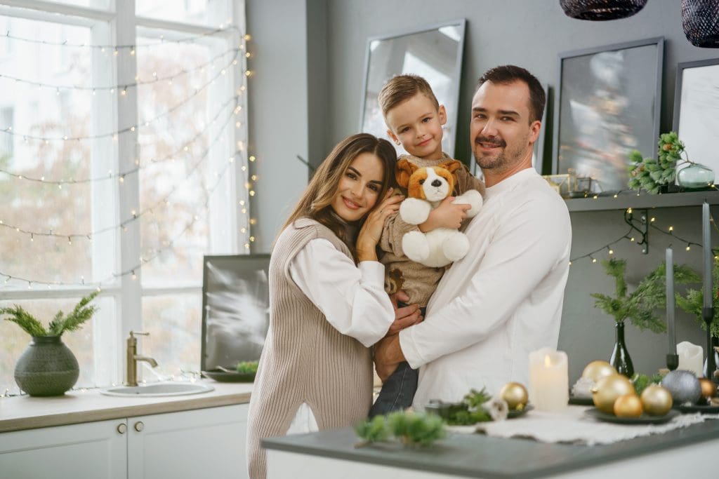 Pregnant mother and father holding their 5-year old son in their brightly-lit kitchen of their new lease to own home in Raleigh, NC