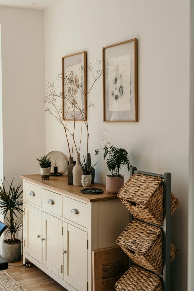 A stylish corner table in a lease to own home in Raleigh NC, decorated with mini vases on top, framed artwork hanging on the wall, and aesthetic wooden bins on the side, creating a warm and inviting space.