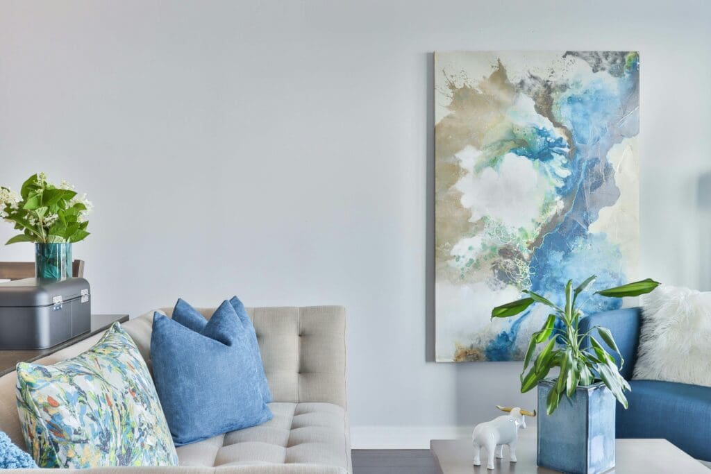 A cozy living room in a lease to own home, with a nice sofa, a beautiful abstract painting hanging on the wall, and a center table with a vase on top. The space exudes a calming ambiance, creating a warm and inviting atmosphere perfect for first-time homebuyers.
