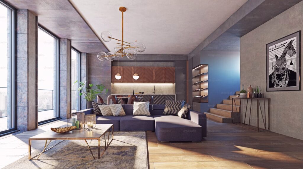 Modern living room with large windows, grey sectional sofa, geometric cushions, sleek coffee table, abstract art, and elegant kitchen in background. Bright and airy.