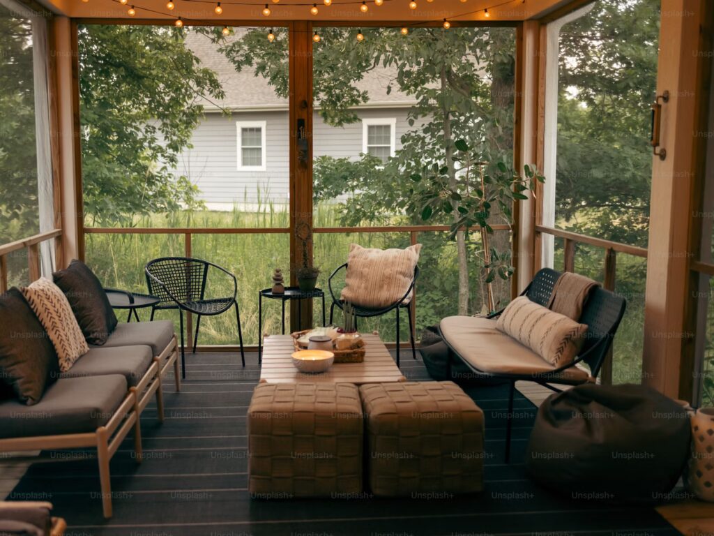 Cozy screened porch with cushioned seating, a coffee table, and string lights. Surrounded by greenery, creating a tranquil, inviting atmosphere.